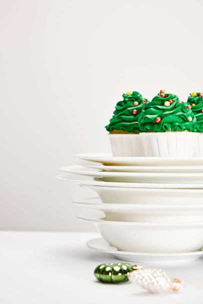 enfoque selectivo de deliciosos cupcakes de árbol de Navidad con platos y bolas brillantes en la superficie blanca aislada en gris
 - Foto, Imagen