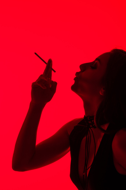 silueta de atractiva chica sexy fumar cigarrillo aislado en rojo
  - Foto, Imagen