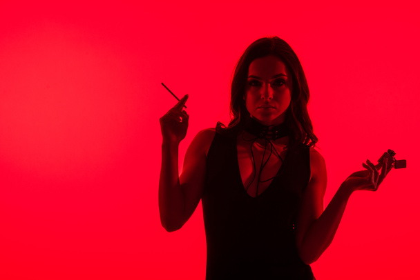 silhouet van mooi sensueel meisje met aansteker roken sigaret geïsoleerd op rood  - Foto, afbeelding