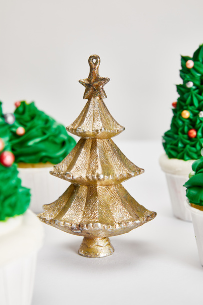 foco selectivo de deliciosos cupcakes y decorativo árbol de Navidad de oro en la superficie blanca aislado en gris
 - Foto, Imagen