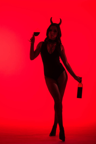 silhouette de fille sexy en costume de diable tenant verre et bouteille de vin, isolé sur rouge
 - Photo, image