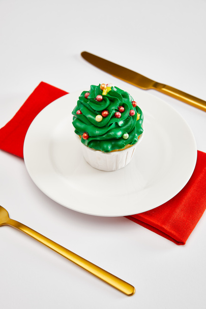 delicioso cupcake en plato blanco con cubiertos de oro y servilleta roja en la superficie blanca
 - Foto, Imagen