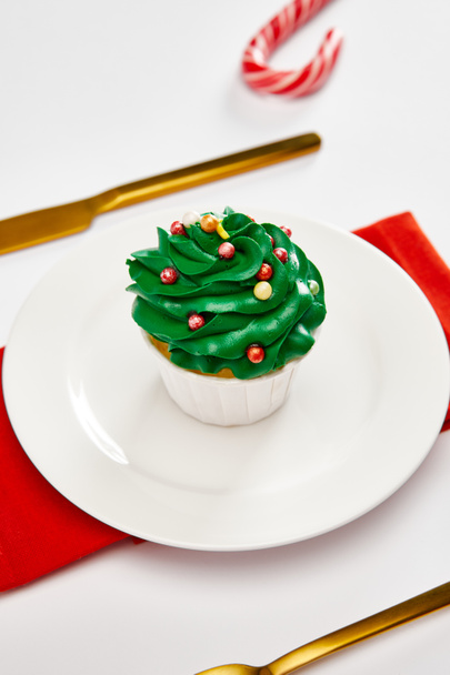 delicioso cupcake en plato blanco con cubiertos de oro y servilleta roja en la superficie blanca
 - Foto, Imagen
