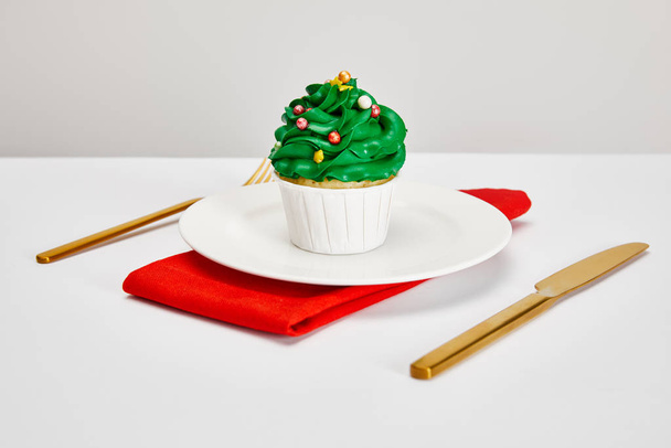 delicioso cupcake en plato blanco con cubiertos de oro y servilleta roja en la superficie blanca aislado en gris
 - Foto, Imagen
