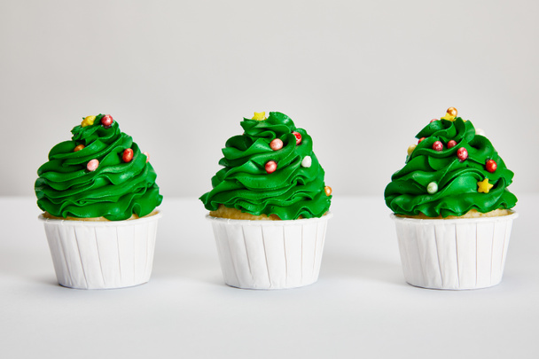 tasty Christmas tree cupcakes in row on white surface isolated on grey - Фото, зображення