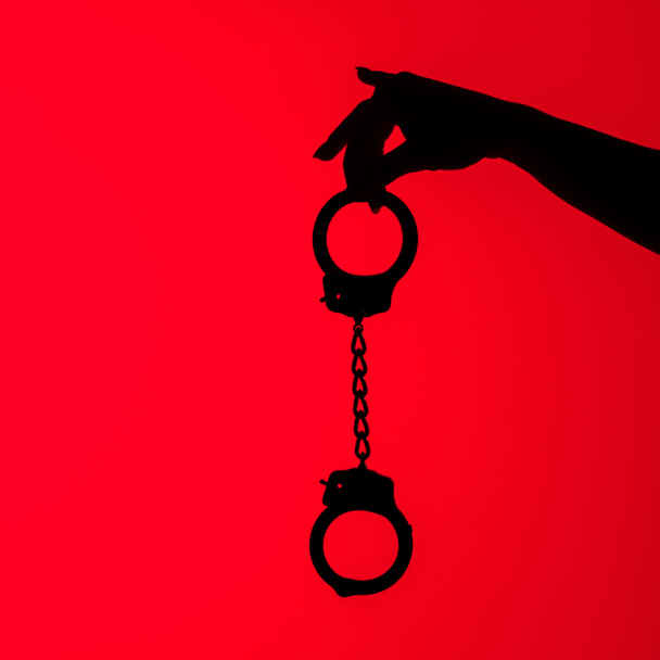 cropped view of silhouette of sexy girl holding handcuff, isolated on red - Фото, изображение