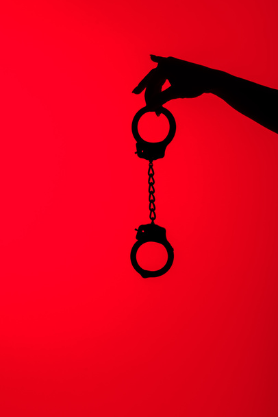 cropped view of silhouette of seductive girl holding handcuff, isolated on red - Foto, Imagem