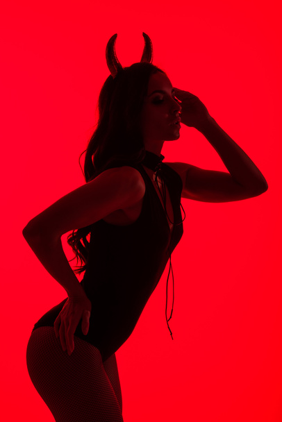 silhouette of sensual woman in Devil costume, isolated on red - Foto, afbeelding
