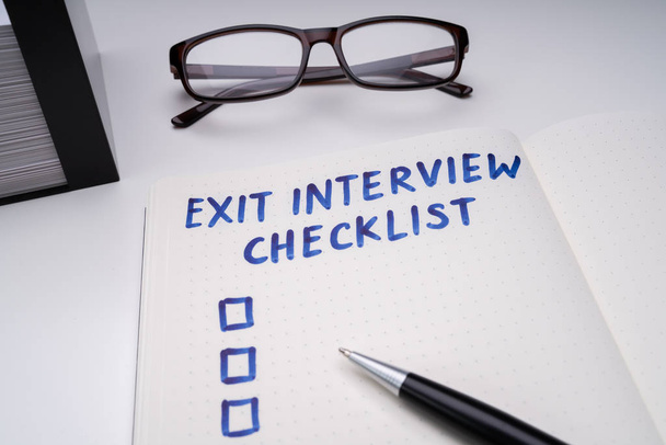 Handwritten Exit Interview Checklist Message On Notebook With Blue Marker And Spectacles Over Office Desk - Photo, Image