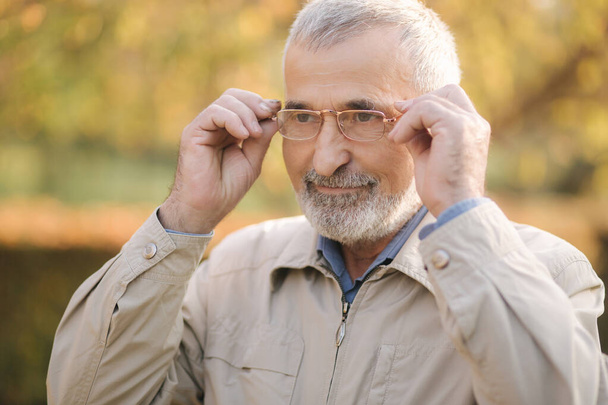 Közelkép jóképű szakállas öregemberről, aki szemüveget visel. Ősz hajú öregember a parkban. - Fotó, kép
