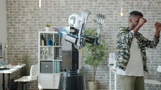 Счастливый инженер танцует в офисе с роботом, весело смеясь и наслаждаясь
 - Кадры, видео