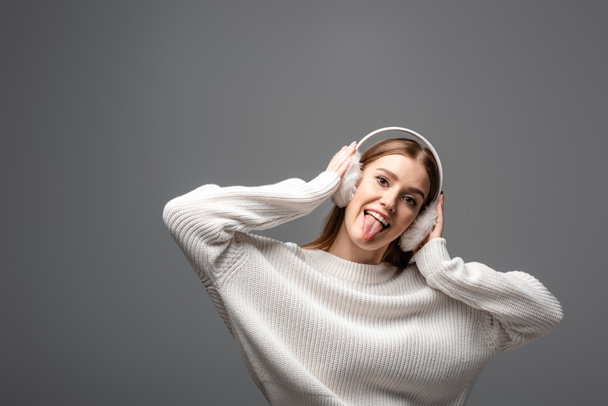 menina engraçada atraente em suéter branco e auriculares furando a língua para fora, isolado em cinza
 - Foto, Imagem