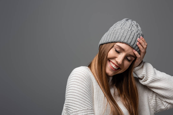 attractive smiling woman in knitted hat and sweater, isolated on grey - Foto, Imagem