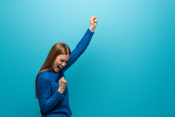 beautiful cheerful woman in blue knitted sweater celebrating triumph, isolated on blue - Fotoğraf, Görsel
