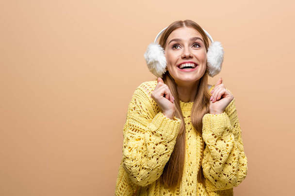 όμορφη ενθουσιασμένοι γυναίκα σε κίτρινο πουλόβερ και τα αυτιά θερμοκοιτίδων, απομονώνονται σε μπεζ - Φωτογραφία, εικόνα