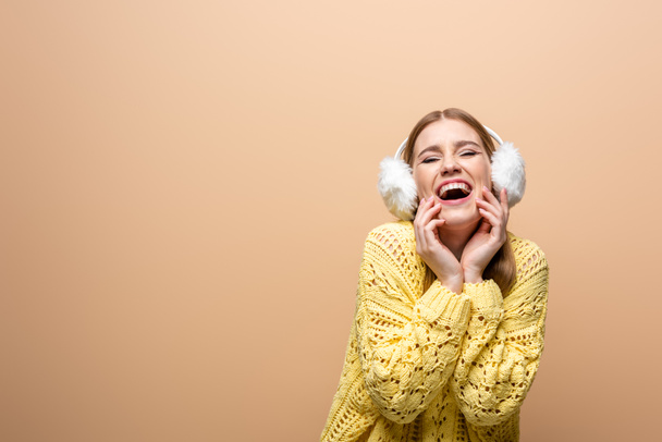 beautiful laughing woman in yellow sweater and earmuffs, isolated on beige - Photo, Image