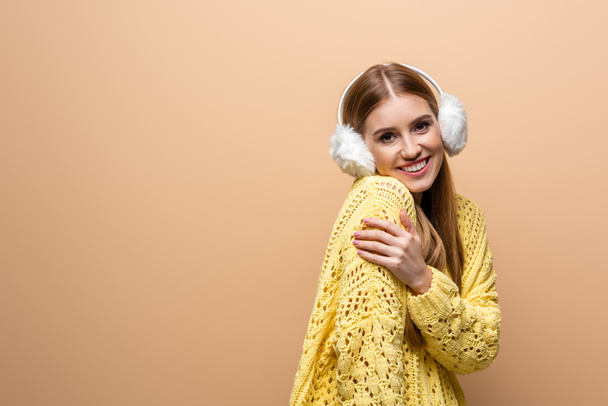 bela mulher fria em suéter amarelo e aquecedores de ouvido, isolado em bege
 - Foto, Imagem