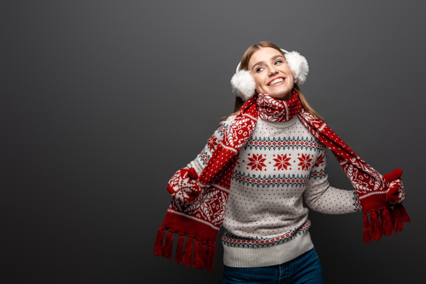 привлекательная улыбающаяся женщина в рождественском свитере, шарфе, рукавицах и наушниках, изолированная на сером
 - Фото, изображение