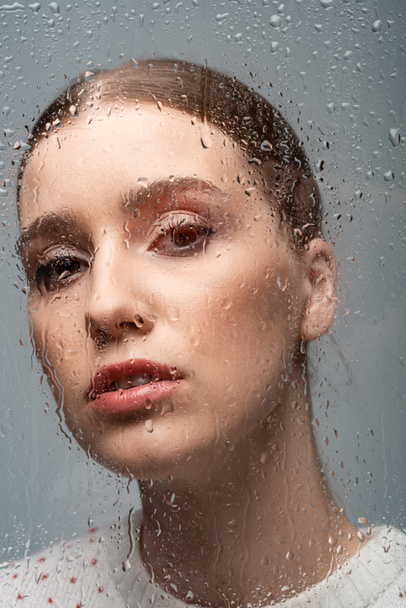 attractive sad woman on grey, beyond wet glass with drops  - Foto, Bild