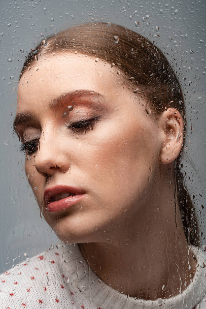 beautiful lonely woman on grey, beyond wet glass with drops  - Foto, imagen