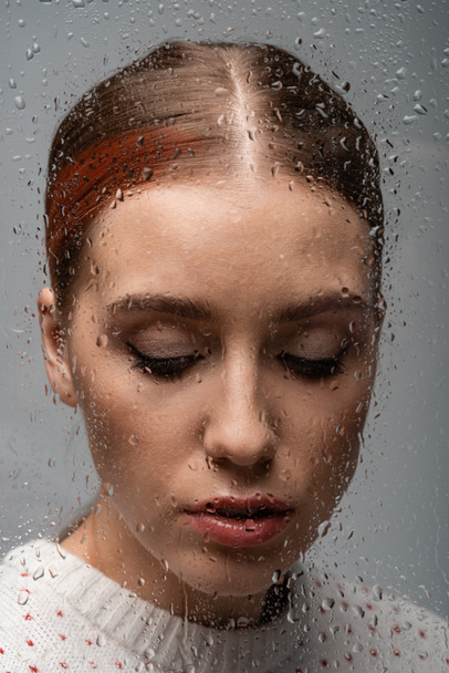 sad lonely woman on grey, beyond wet glass with drops  - Fotó, kép