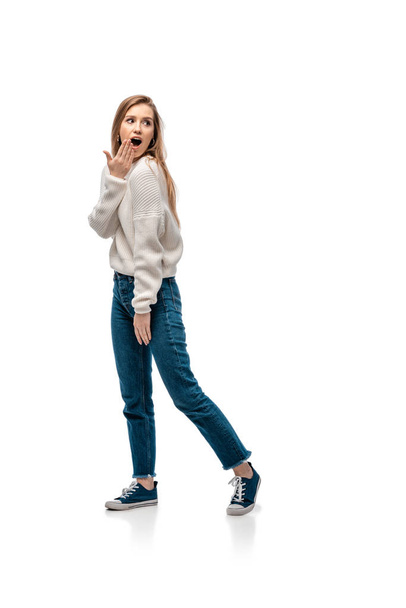 mooie geschokte vrouw in jeans en witte trui, geïsoleerd op wit - Foto, afbeelding