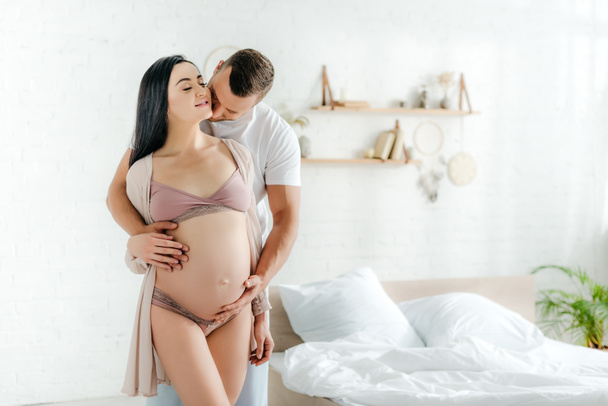 happy husband hugging and kissing his beautiful pregnant wife in bed - Photo, Image