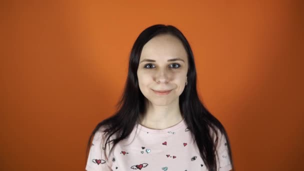 Beautiful woman smiling looking at the camera standing on an orange background. - Кадры, видео