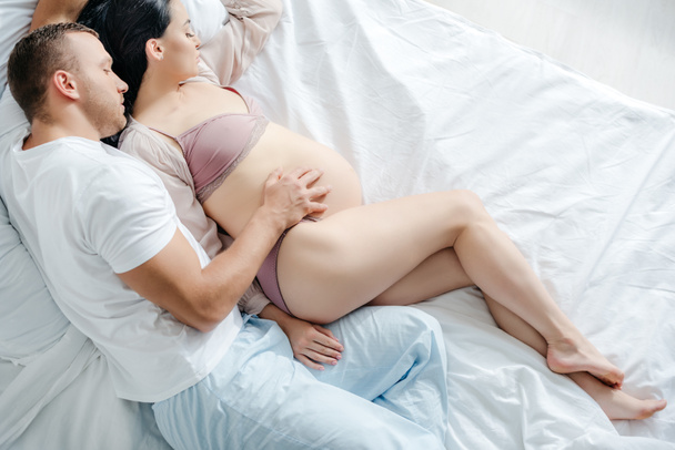 ベッドに横になって妊娠中の妻を抱きしめる夫の姿  - 写真・画像