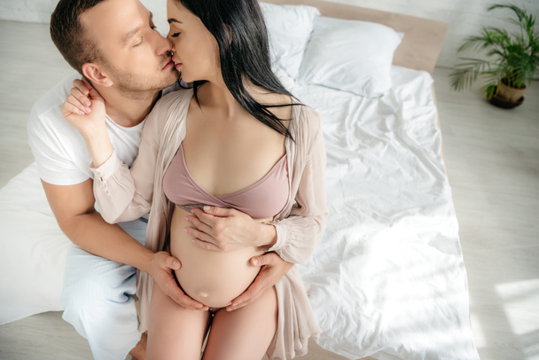 happy husband hugging and kissing his pregnant wife in bed - Fotó, kép