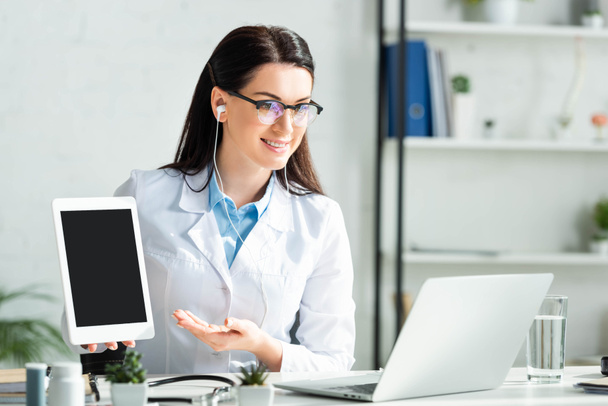 médecin souriant montrant le diagnostic sur tablette numérique tout en ayant une consultation en ligne sur ordinateur portable
  - Photo, image