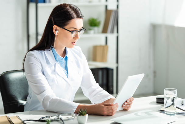 érdeklődő orvos fülhallgató, amely online konzultáció a digitális tabletta klinika irodájában laptop - Fotó, kép