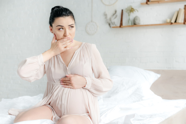 ベッドに座りながら吐き気を催す夜の魅力的な妊婦 - 写真・画像