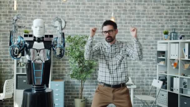 Cheerful office worker dancing with robot at work having fun enjoying break - Felvétel, videó