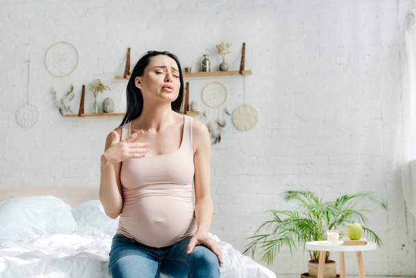 όμορφη αναστατωμένη έγκυος γυναίκα που έχει πόνο ενώ κάθεται στο κρεβάτι  - Φωτογραφία, εικόνα