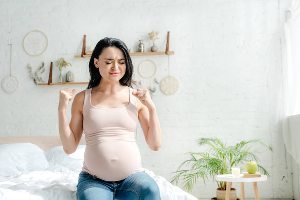 emotional pregnant woman holding fists in bedroom - Foto, imagen