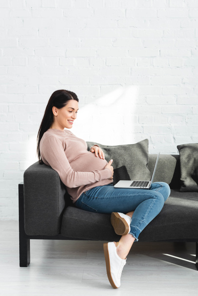 улыбающаяся беременная женщина, имеющая онлайн консультации с врачом на ноутбуке дома
 - Фото, изображение