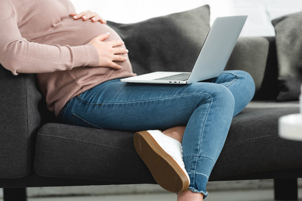 cropped view of pregnant woman touching belly and having online consultation with doctor on laptop at home  - Фото, зображення