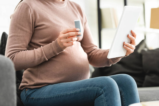 cropped view of pregnant patient holding pills while having online consultation with doctor on digital tablet at home  - Φωτογραφία, εικόνα