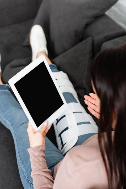 vágott kilátás nő törött lábbal, amelynek online konzultáció orvos digitális tabletta, miközben ül a kanapén - Fotó, kép