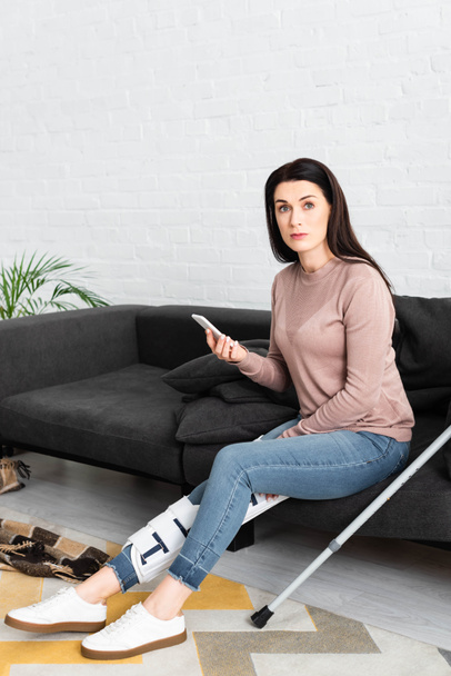femme avec jambe cassée et béquilles ayant une consultation en ligne avec un médecin sur smartphone sur canapé
 - Photo, image
