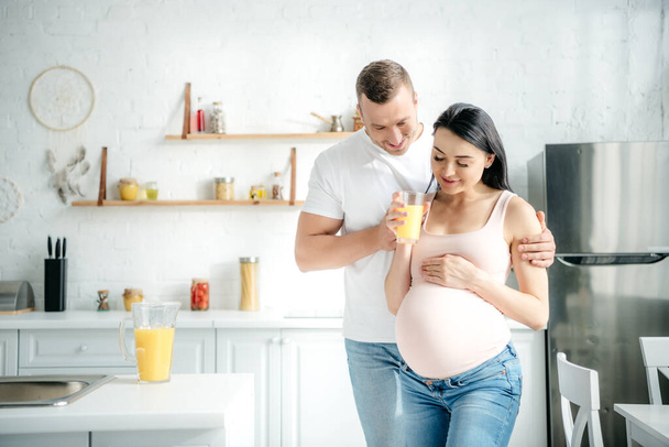 happy beautiful pregnant couple holding orange juice in kitchen - Foto, Imagen