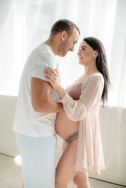 счастливый муж обнимает свою улыбающуюся беременную жену
 - Фото, изображение