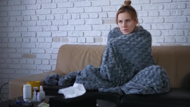 Shot of sick young caucasian women feels cold and trembling at home covering with warm grey plaid blanket shivering sitting on couch got flu influenza virus grippe symptoms concept - Footage, Video