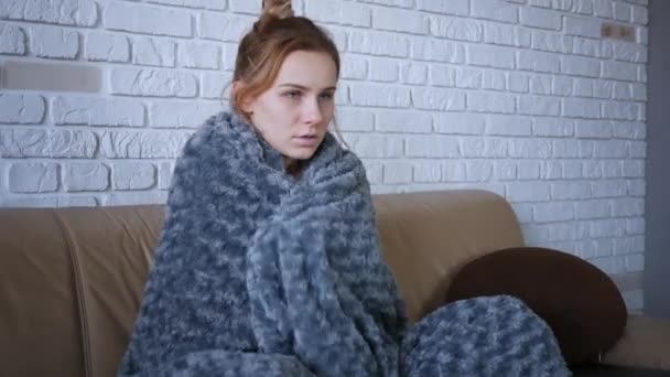 Shot of sick young caucasian women feels cold and trembling at home covering with warm grey plaid blanket shivering sitting on couch got flu influenza virus grippe symptoms concept - Footage, Video