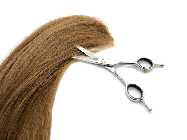 Hairdressing scissors and hair isolated on a white background. Composition of metal scissors and brown hair. Professional scissors. Women's hair. Composition for a beauty salon - Photo, Image