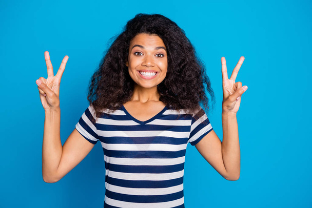 Photo of cheerful positive nice pretty cute charming girlfriend showing you double v-sign showing her white teeth in striped t-shirt isolated vivid color blue background - Foto, Imagen