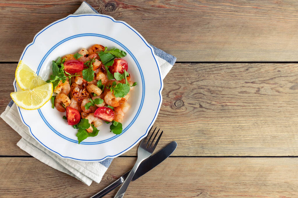 Fresh homemade salad of shrimp, arugula and tomato in a white plate on a wooden table, top view, flat lay, copyspace - Foto, Bild