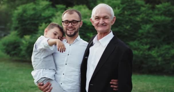 Charismatický a usměvavý starý muž se svým synem a vnukem před kamerou uprostřed parku, užívající si čas s rodinou - Záběry, video