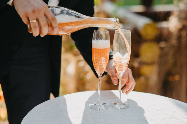 Мужская рука наливает шампанское в бокалы для вина на стол
. - Фото, изображение